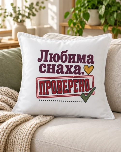 Бяла възглавница със зелена отметка, печат, сърце и надпис Любима снаха – на дивана